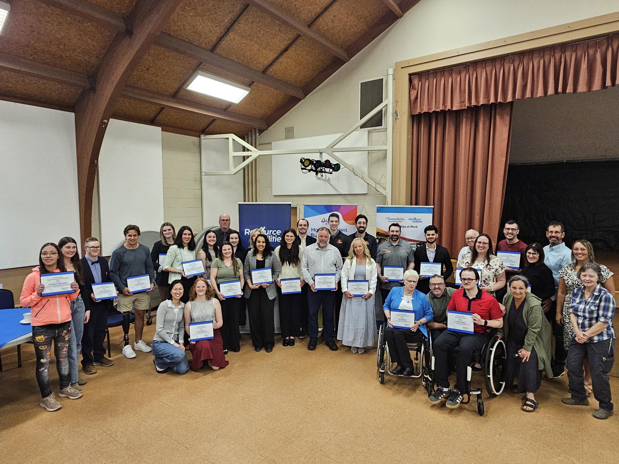 A group of people holding up award plaques looking pround and smiling in front of a stage
